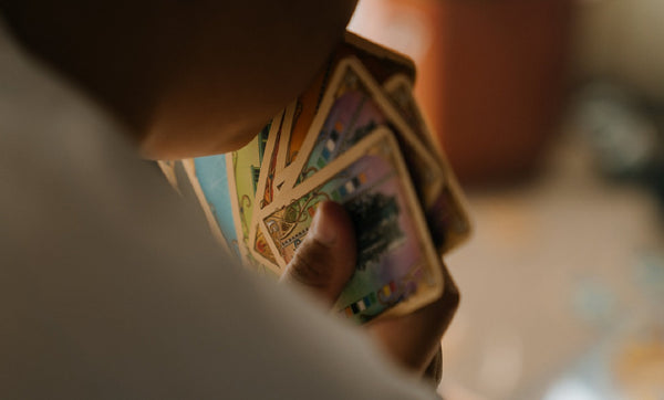 A photo of a person holding a hand of cards, shot from behind. You can see the curve of the person's chin, their shoulder, and a number of colorful cards spread out in their hand