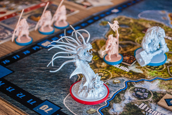 A photograph of a boardgame. There are several pieces, which look like humanoid explorers in red, and sea monsters in blue. They are set on a board that looks like a map with both land and sea depicted on it. 