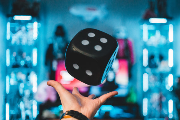 A photograph of a hand throwing up a large black die against a blue-lit background