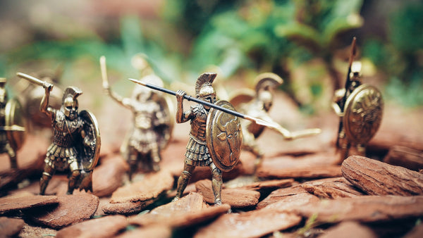 A photograph of severarl miniature roman figures holding spears and wearing hoplite armor, arranged as though they are walking over a mountain