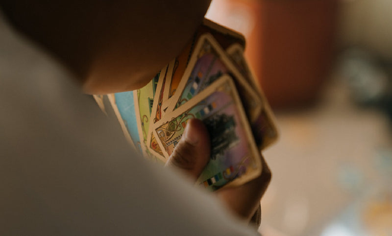 A photo of a person holding a hand of cards, shot from behind. You can see the curve of the person's chin, their shoulder, and a number of colorful cards spread out in their hand