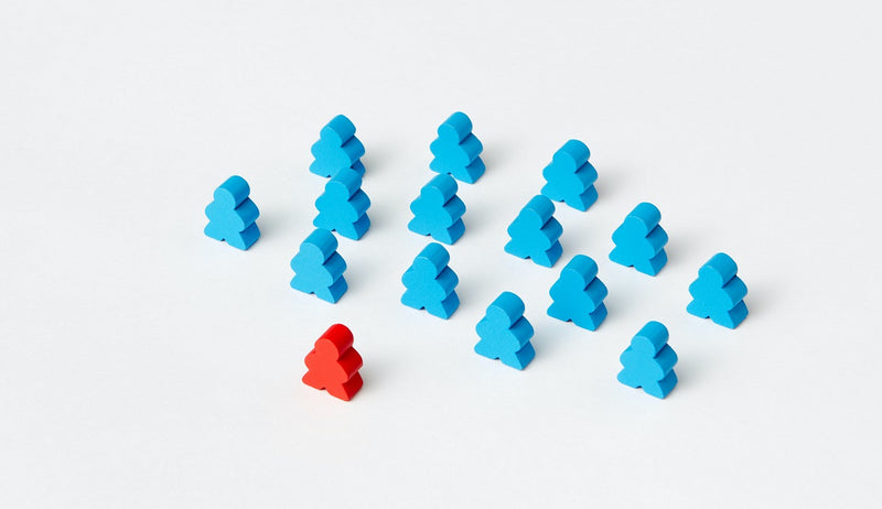 A photo of a number of meeples standing on a white surface. Several blue meeples are standing in a spread formation behind a single red meeple