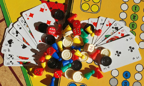 A photo of a pile of dice, cards, tokens, and pegs on a colorful lettered and numbered background