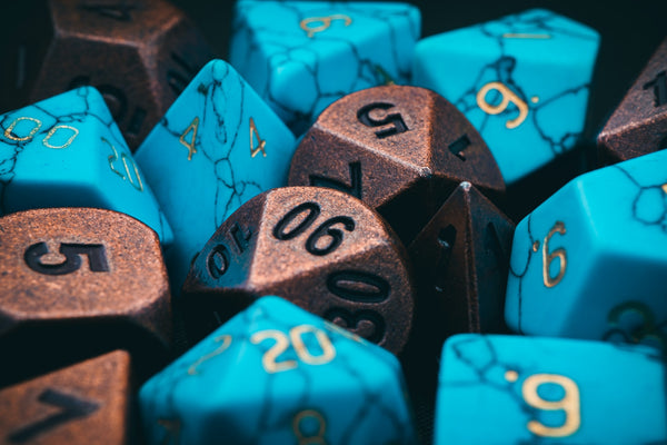 A photo of dice, one set in marbled blue with gold numbers, and one set in copper with black numbers, jumbled together